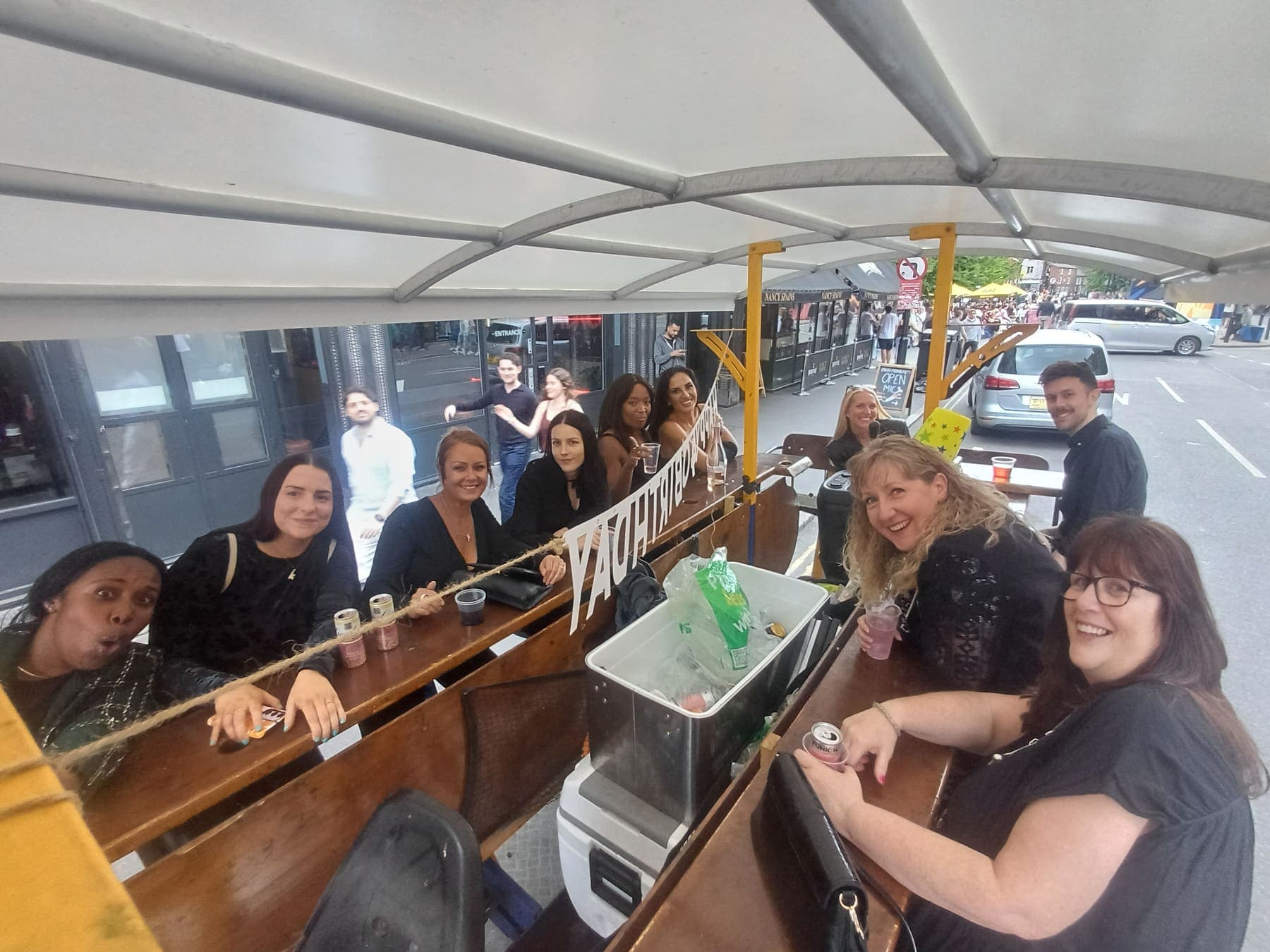 A group of friends raising drinks around the bar on board the PedalCity party bike as it rolls through Manchester